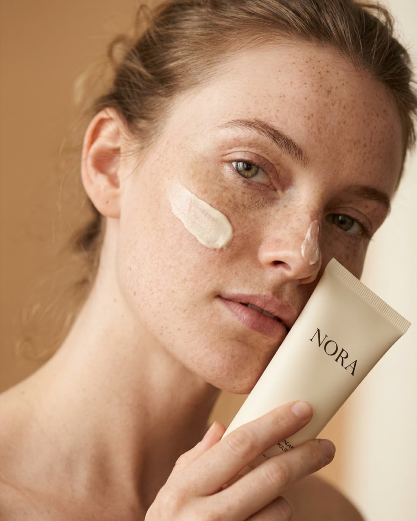 Cream face moisturizer in hand, freckled model, neutral linen